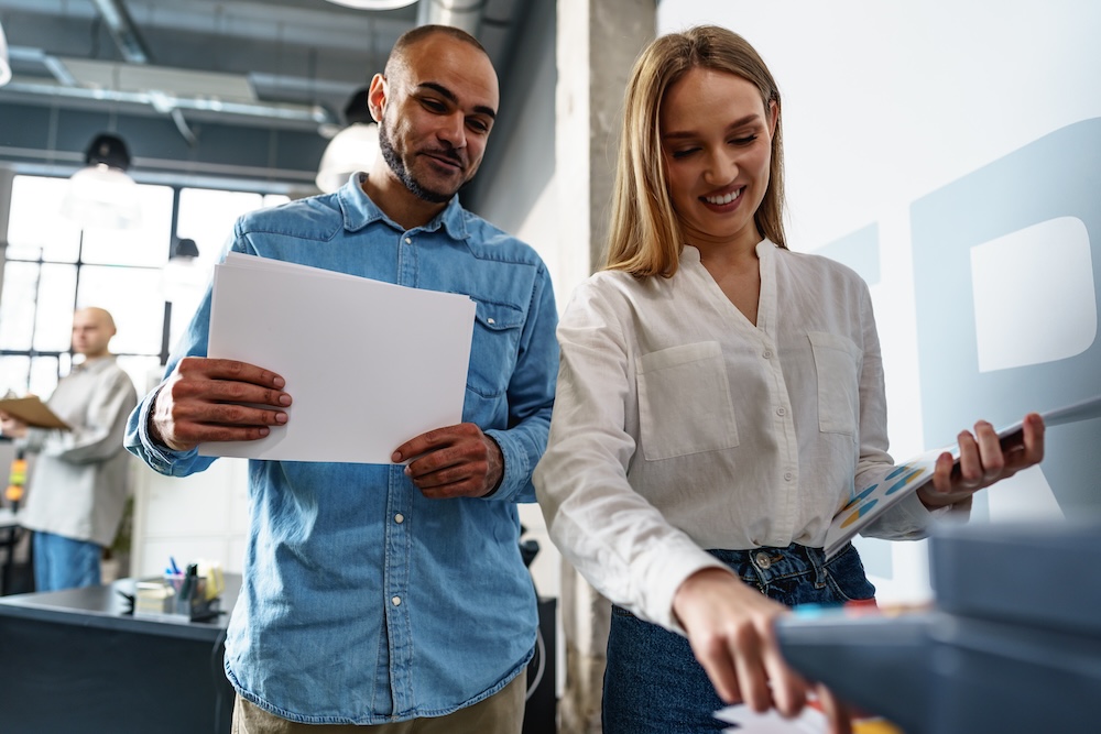 Two employees using new modern printer in office, technology solutions concept