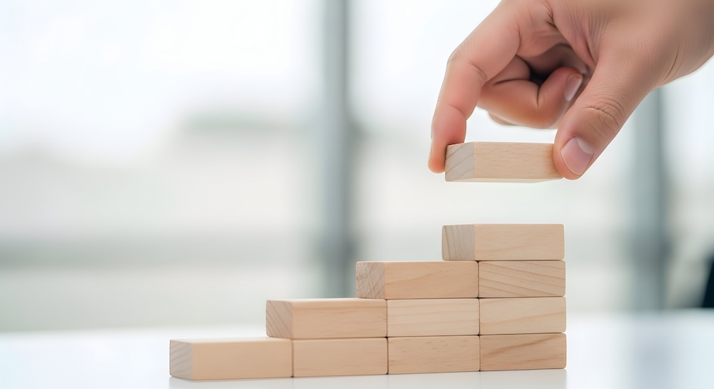 Hand aligning wooden blocks in step formation, startup growth concept, pastel blurred background