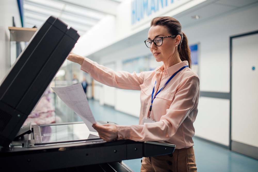 Teacher is printing off work sheets for her next lesson using the printer in the school hall. Concept of managed printing in schools.