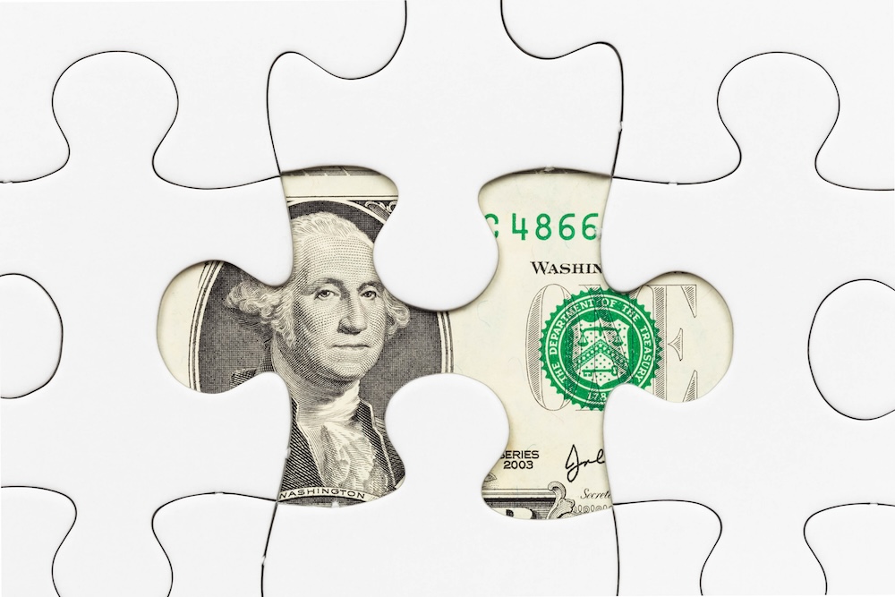US dollar banknote hidden under puzzle financial concept. Suggests hidden costs.